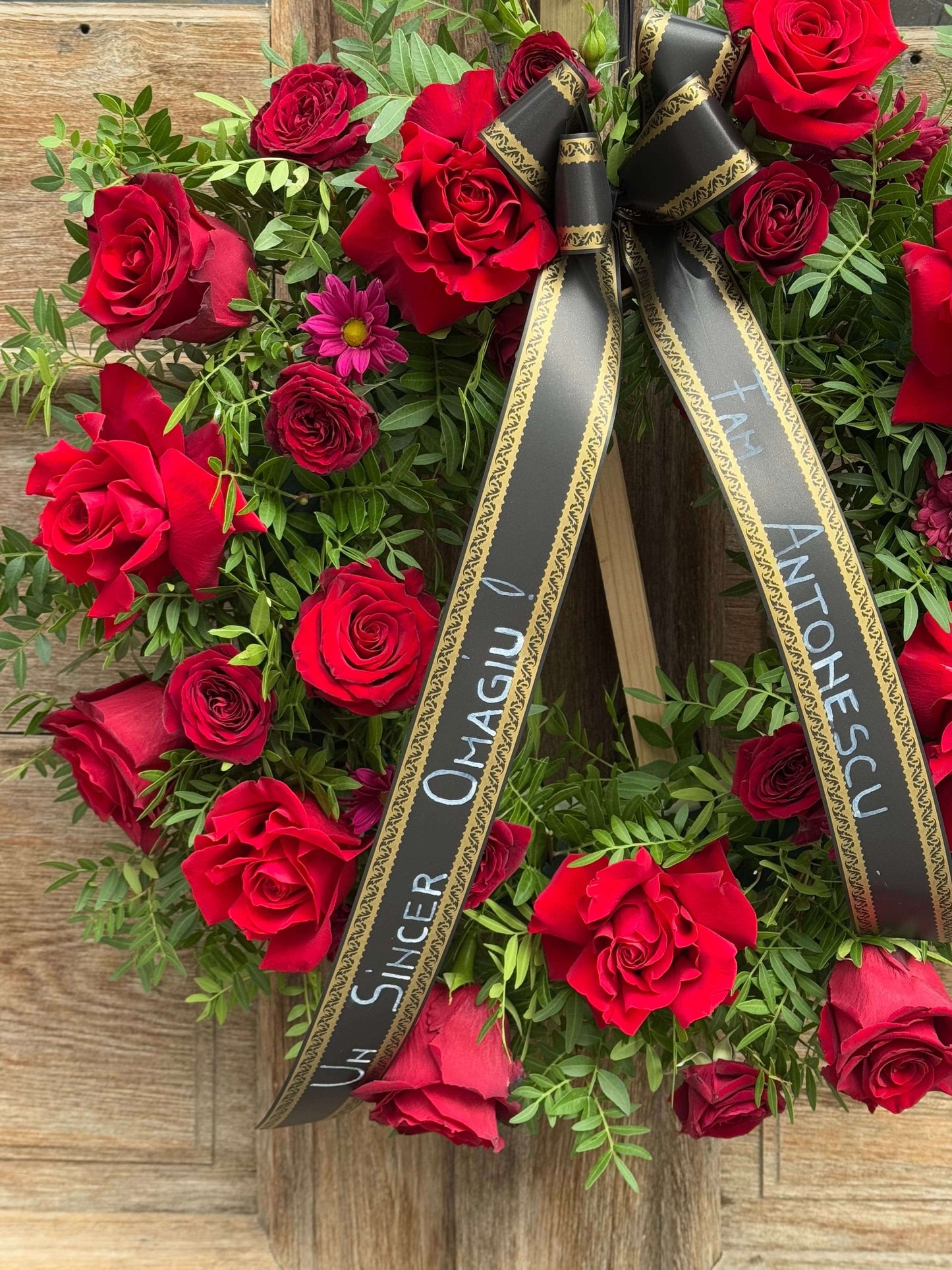 Coroană funerară dedicată cu flori roșii și panglici personalizate, omagiu floral sincer pentru cei dragi.